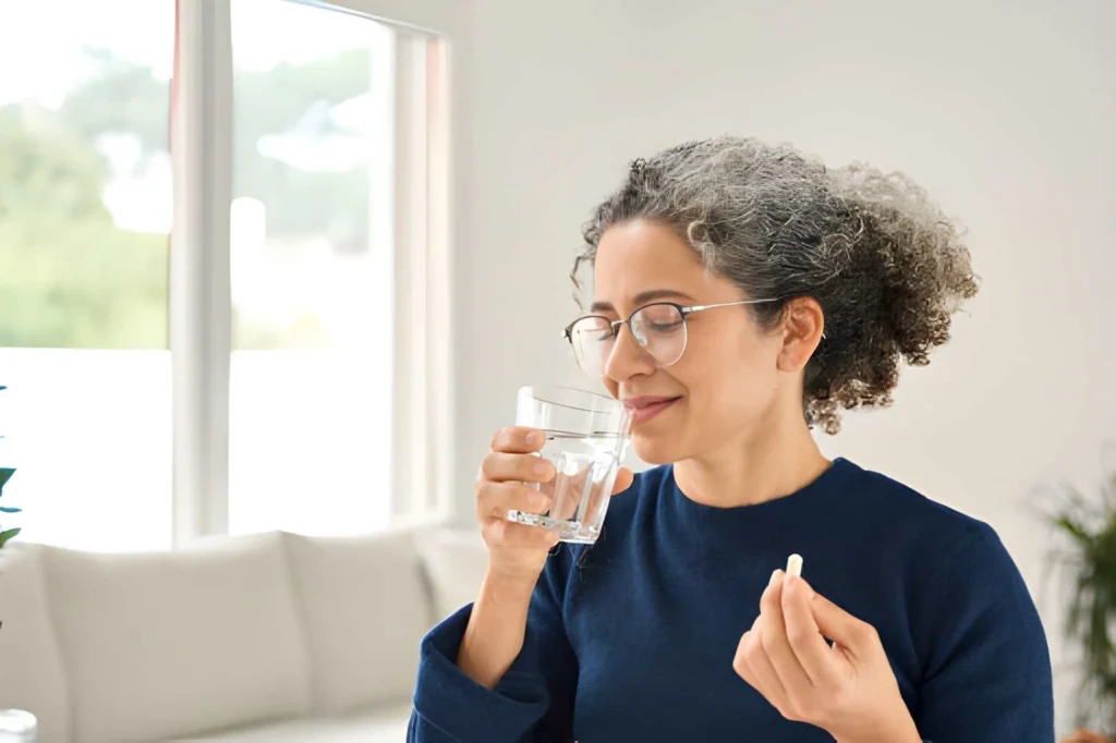 Eine gesunde Frau mittleren Alters, die zu Hause über eine Tablette spricht und ein Glas Wasser in der Hand hält